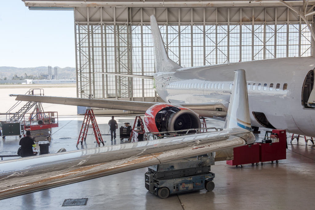 A photo of a maintenance repair and overhaul hangar with aircraft, tools and a aircraft mechanic