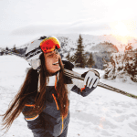 A happy woman standing in snowy mountains holding her snow skis